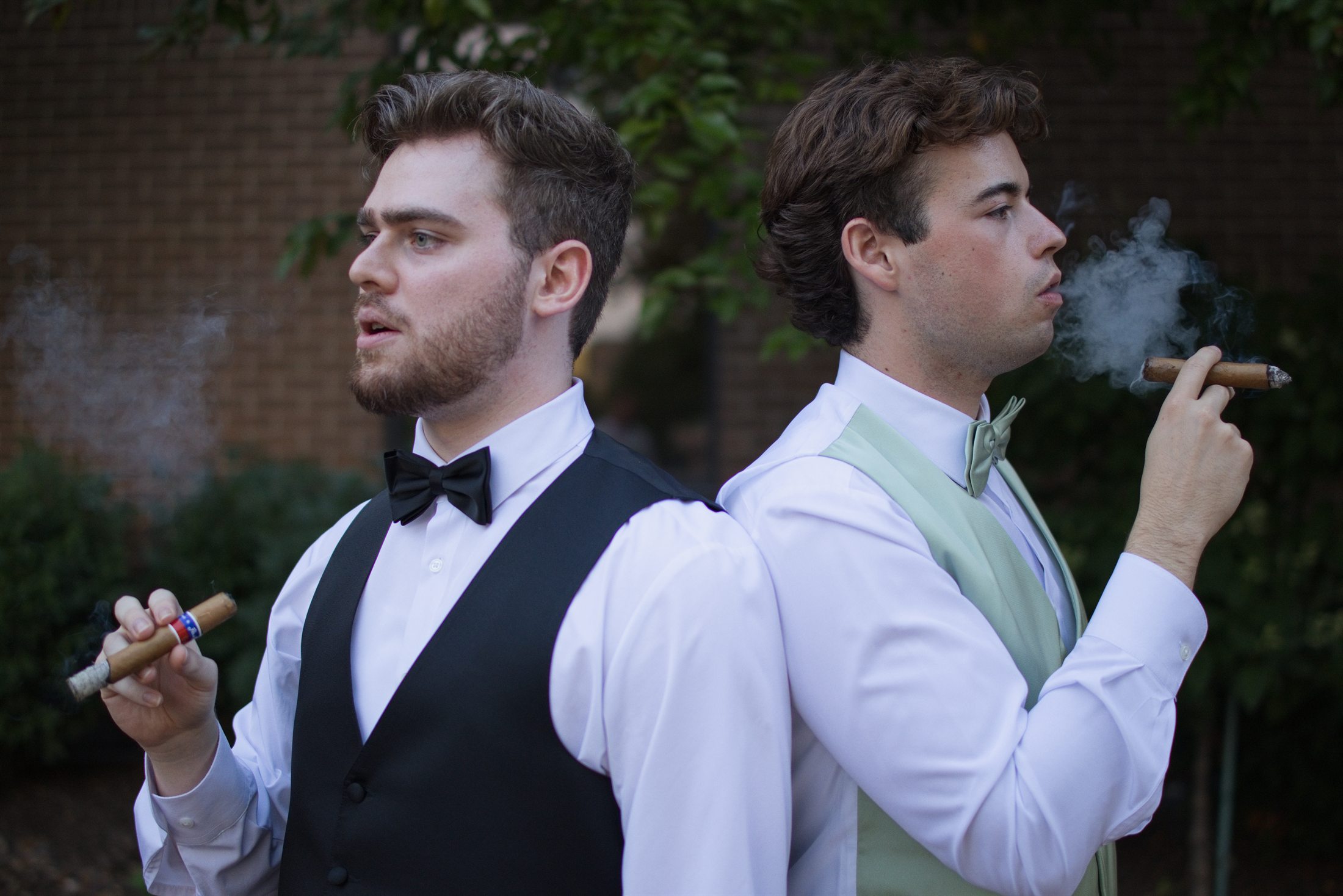 Brennan and a groomsman standing back-to-back with celebratory cigars